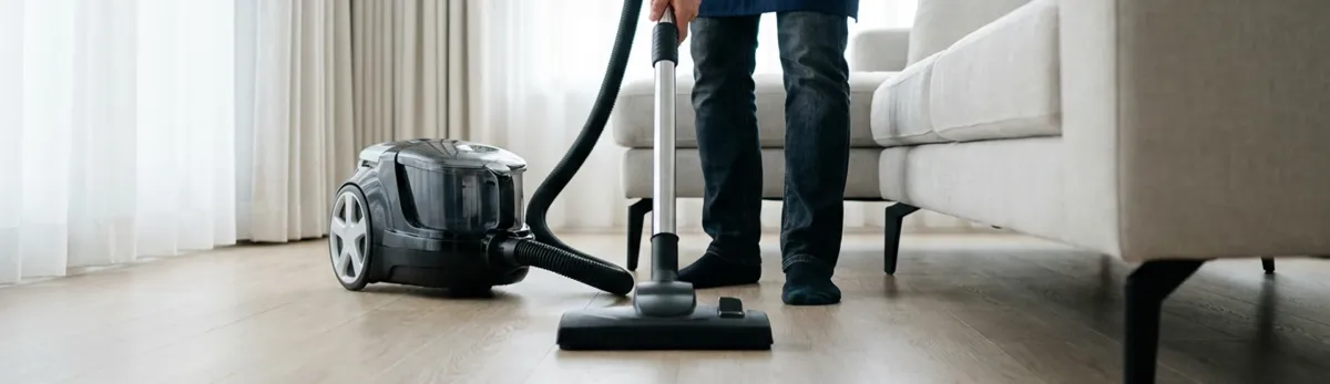Professional house cleaner vacuuming a living room floor with a canister vacuum cleaner, Richmond, VA.